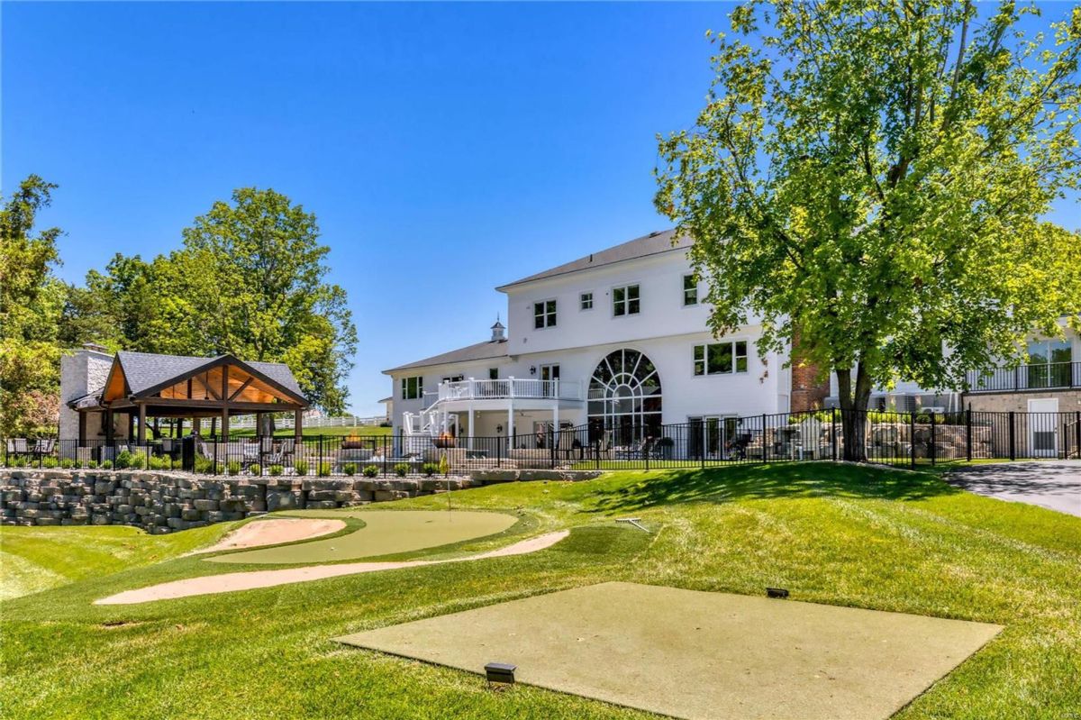 A putting green is situated on a grassy area in front of a large white house. 