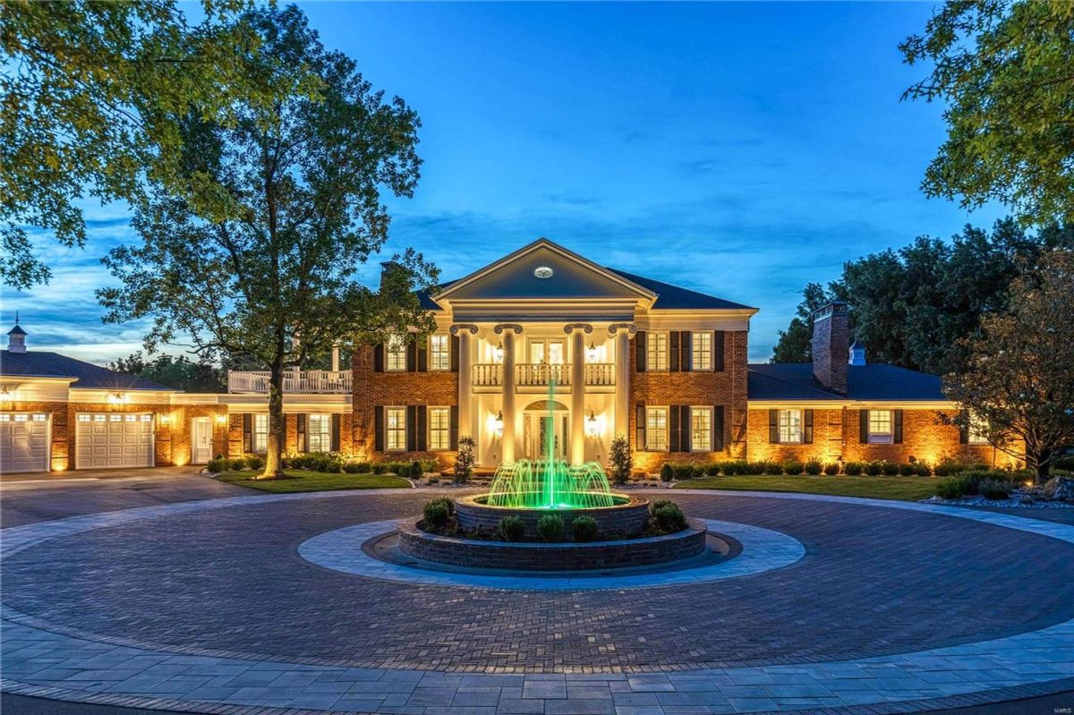 Large brick home with white columns and a circular driveway is shown at night.