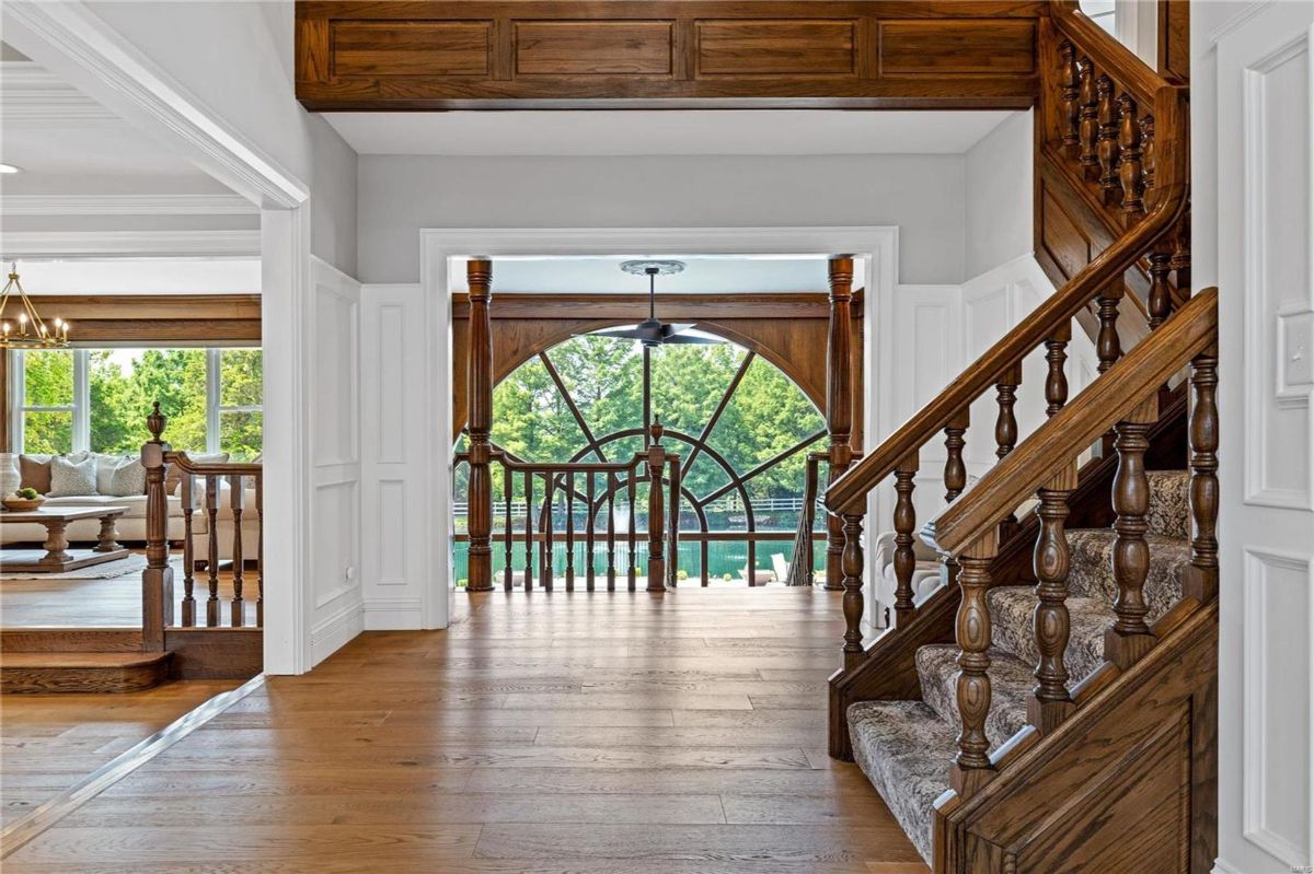 Grand foyer with hardwood floors features a large arched window looking out onto a water feature. 