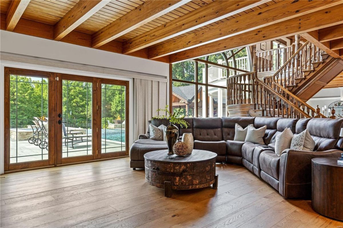 A living room, showcasing hardwood floors and exposed wood beams, centers around a sizable sectional sofa and a circular coffee table. 