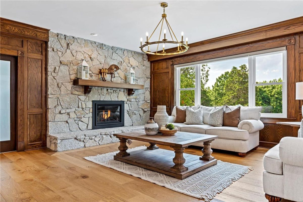 This living area features a rustic stone fireplace, hardwood floors, and large windows offering scenic views. 