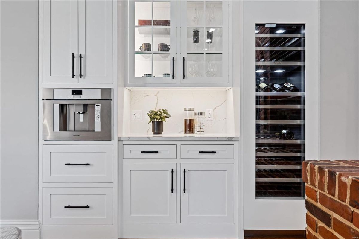 White cabinetry with black hardware incorporates a built-in coffee maker and a wine refrigerator.