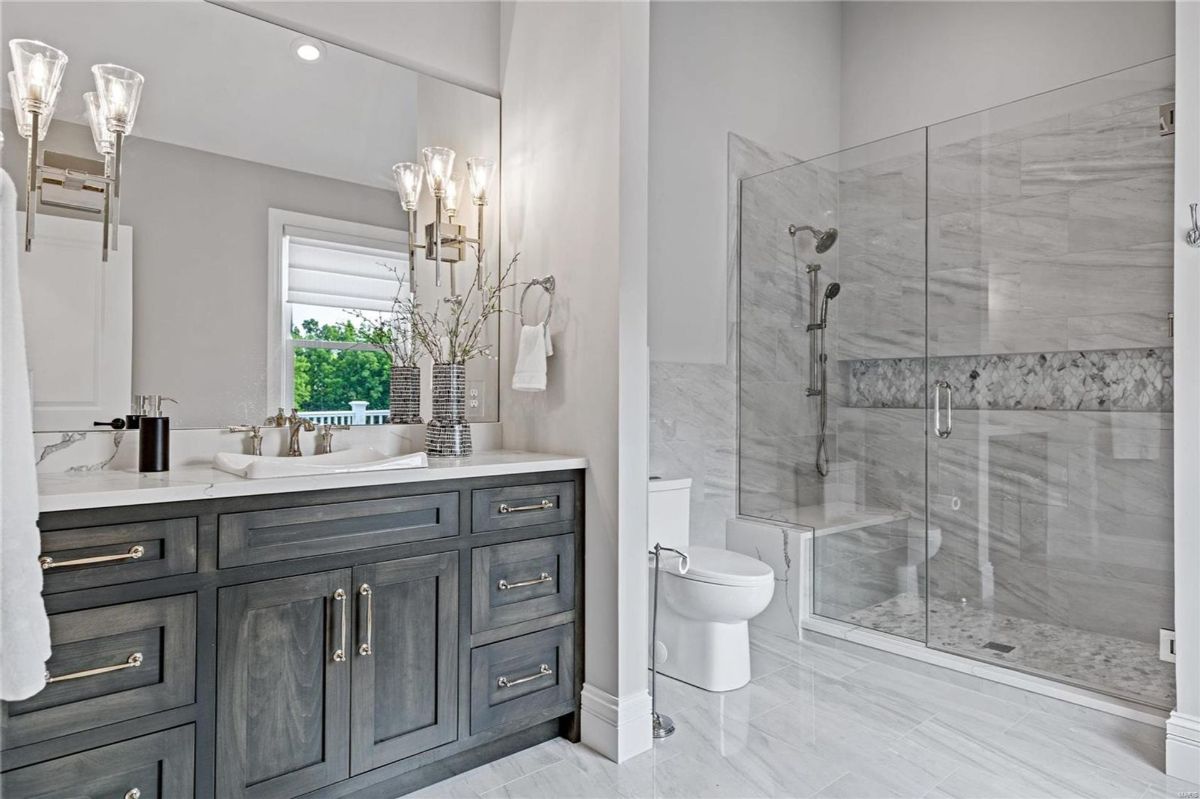 A modern bathroom features a dark gray wood vanity with a white marble countertop and brushed gold hardware. 