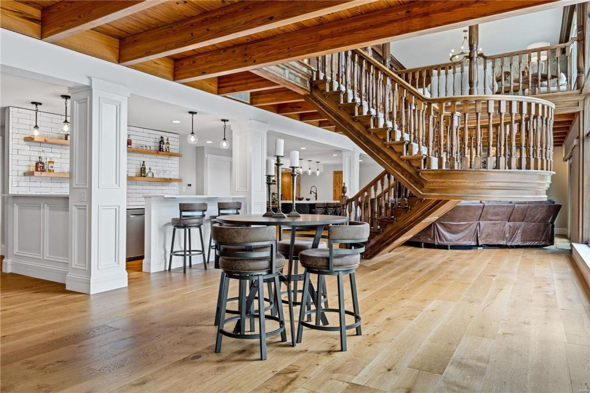 Open space features hardwood floors, exposed wood beams, and a grand wooden staircase. 