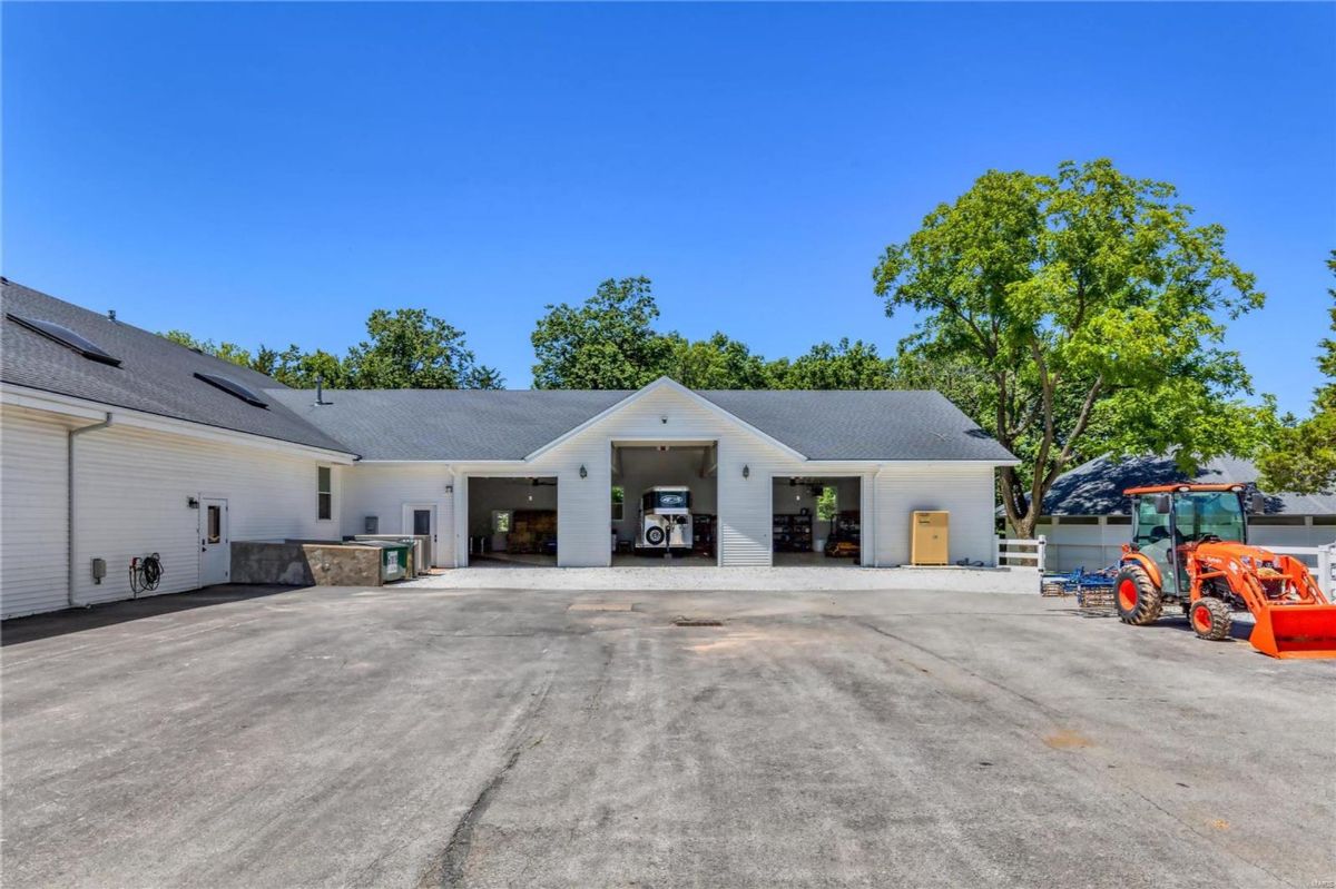  White building with multiple garage doors is situated in a rural setting. 