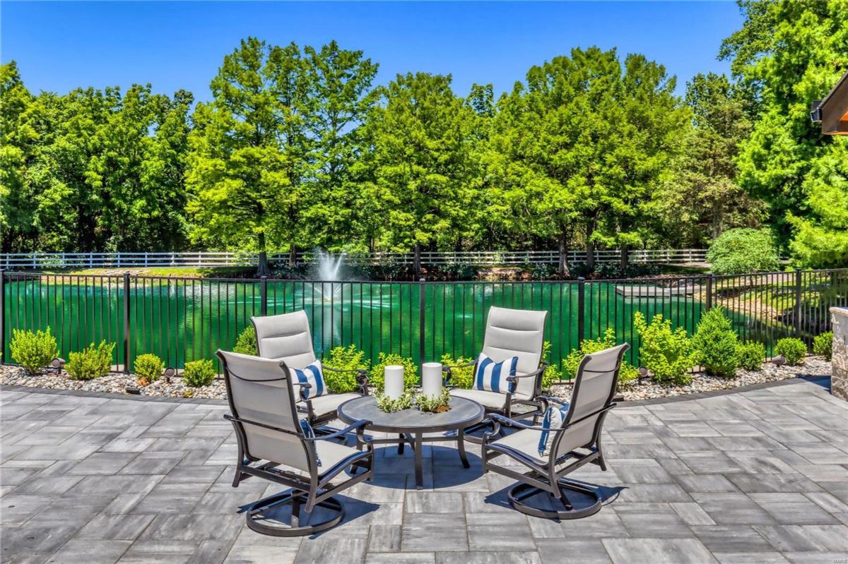 Patio with a gray stone surface overlooks a pond. Four swivel chairs surround a round table, creating a comfortable seating area. 