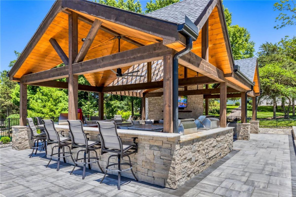 Outdoor kitchen and dining pavilion features a stone countertop, built-in grills, and bar seating.