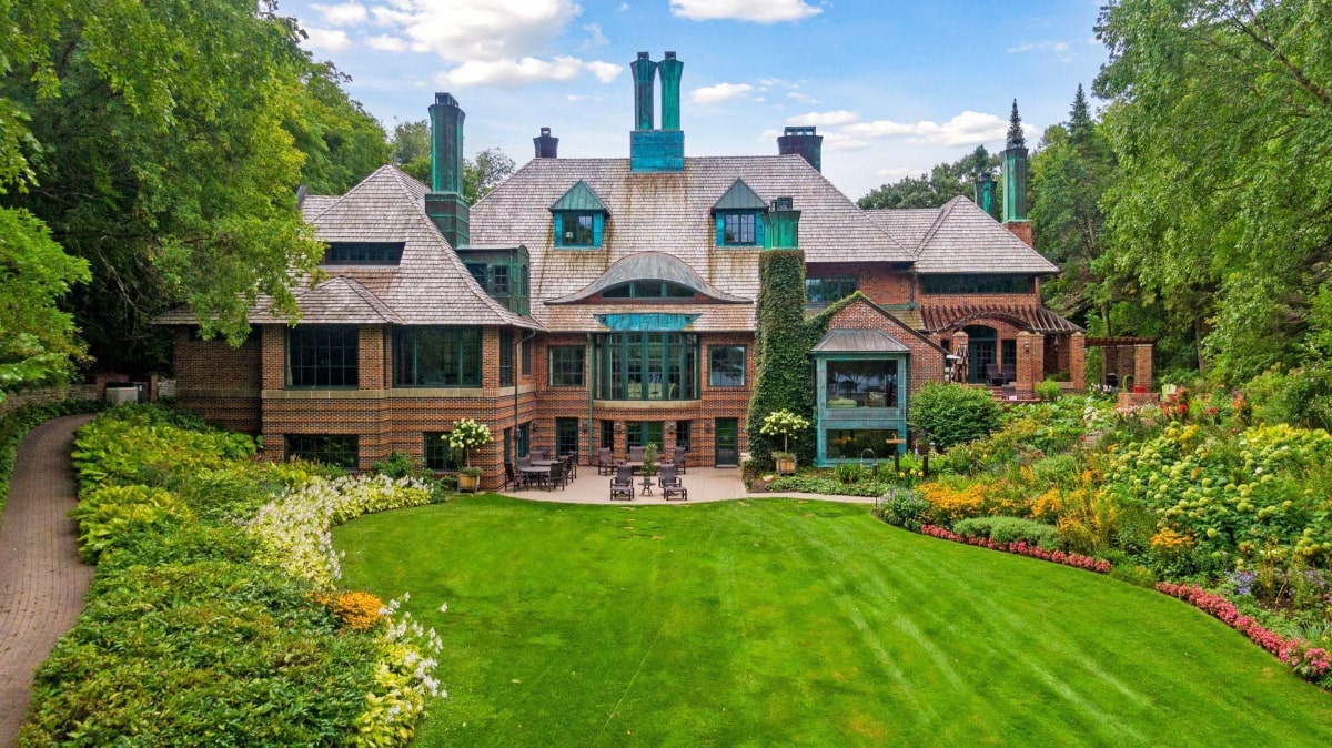 Brick mansion that has a sprawling lawn and meticulously landscaped gardens.