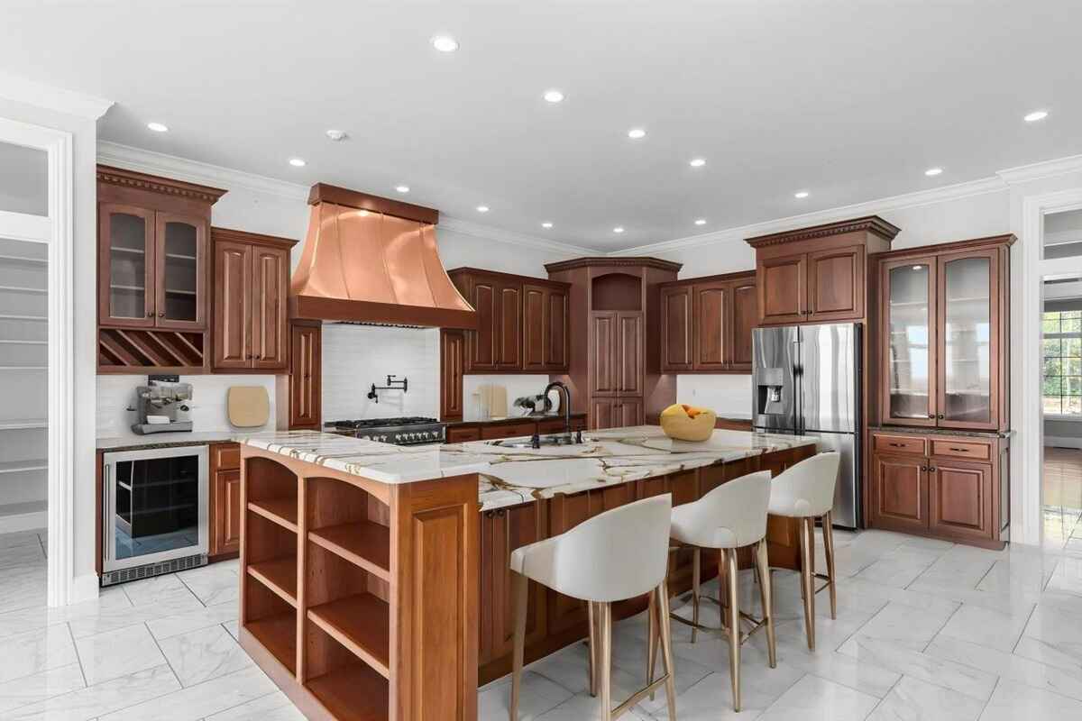 Kitchen is equipped with wooden cabinetry, marble countertops, a copper range hood, and modern appliances.