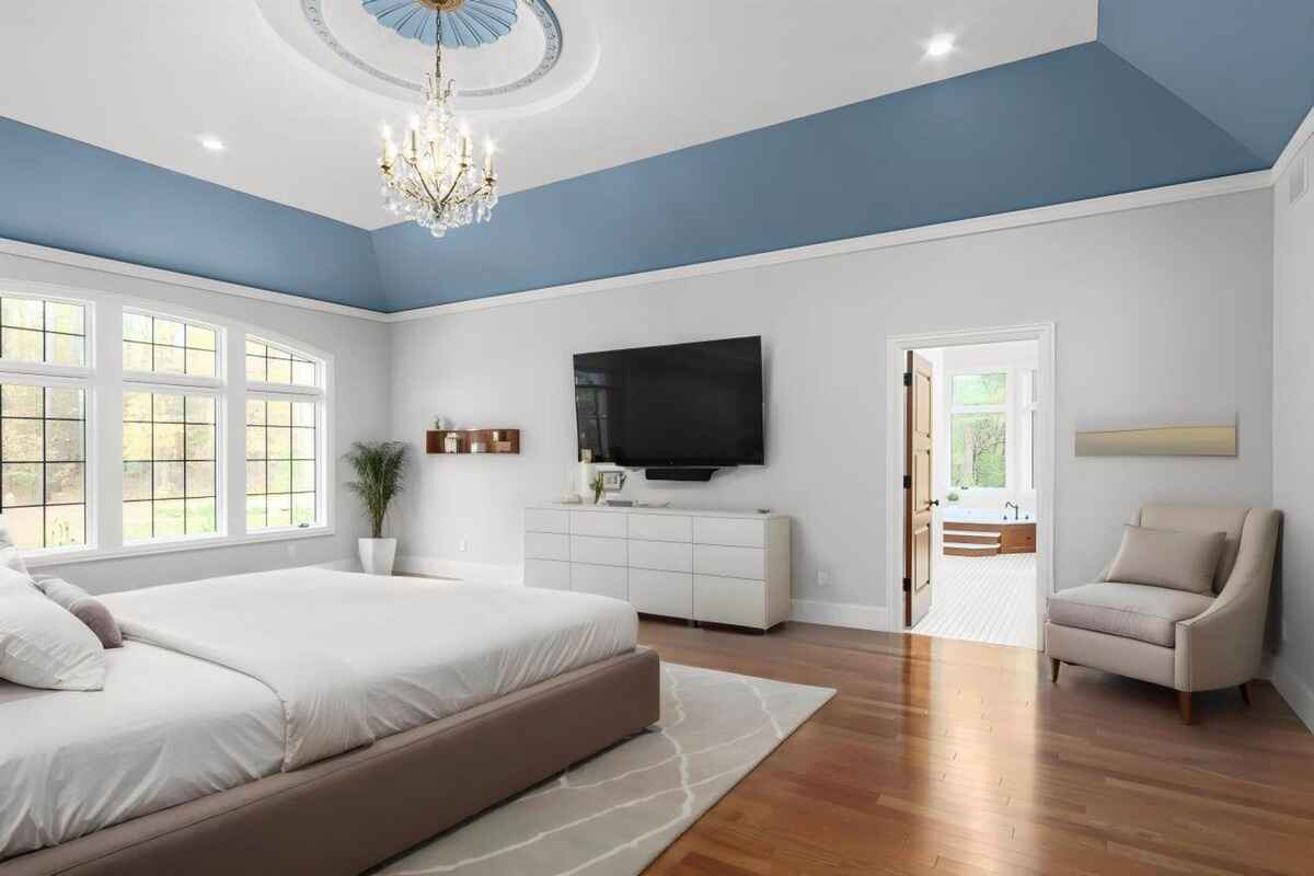 Master bedroom includes large windows, a chandelier, a blue tray ceiling, and an en-suite bathroom entrance.