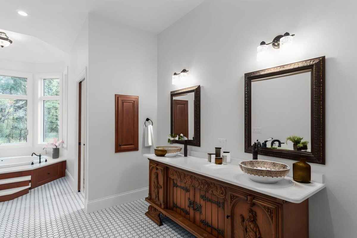 Bathroom displays dual vanity with carved wooden cabinets, framed mirrors, and a soaking tub near a window.