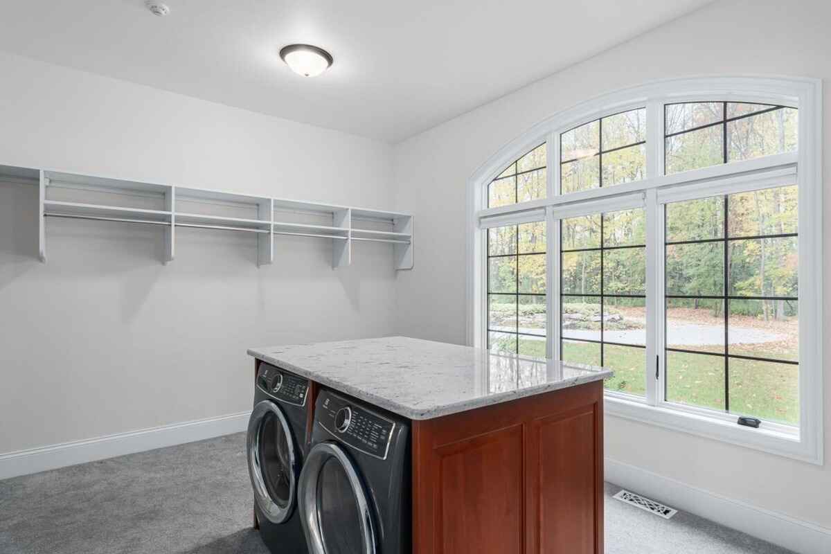 Laundry room includes a central countertop island, front-loading washer and dryer, and built-in shelving.