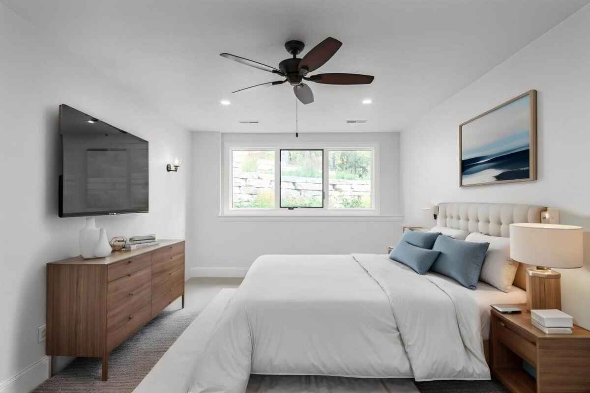 Guest bedroom includes a ceiling fan, a mounted television, and a window overlooking an outdoor rock wall.