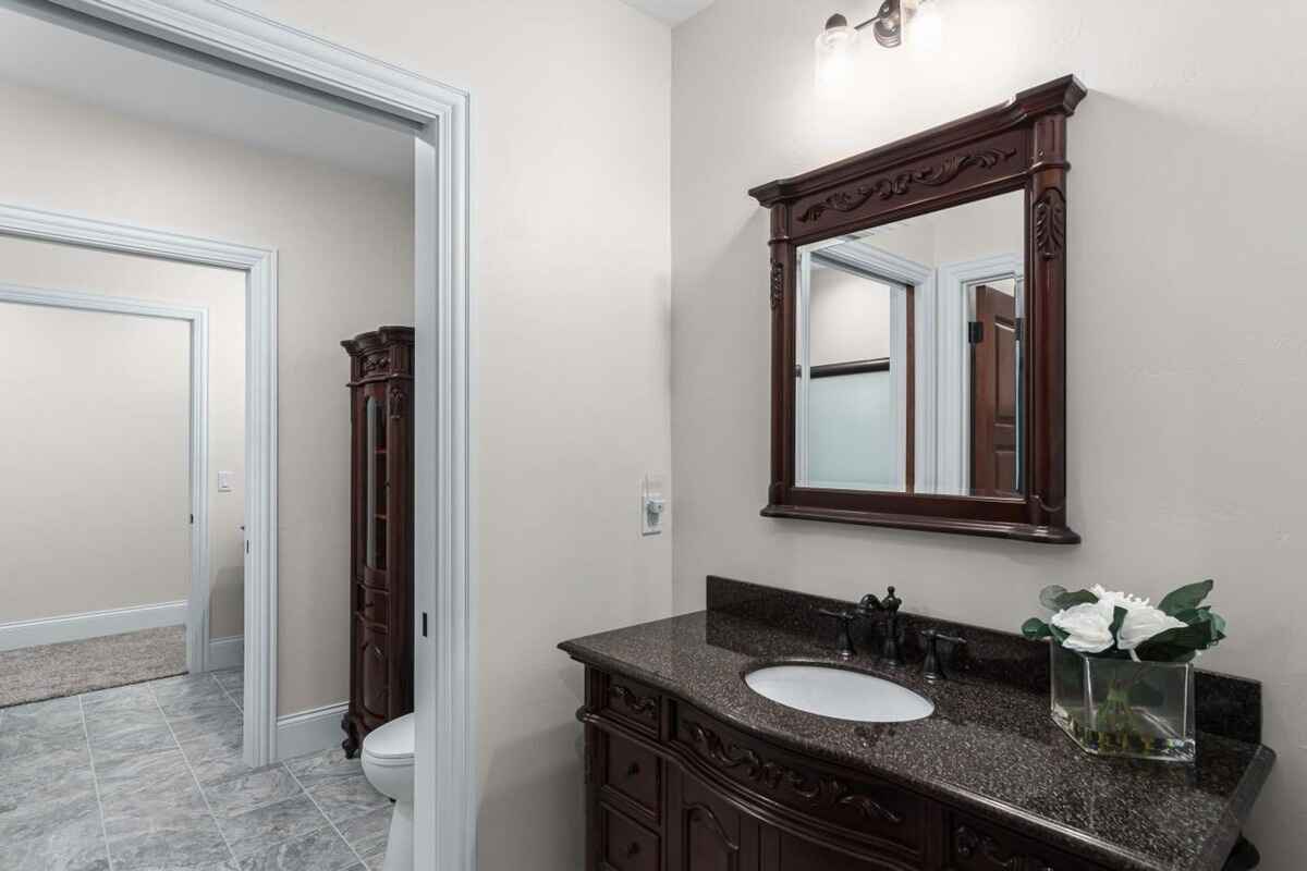 Bathroom has dark granite counters, a framed mirror, and tiled flooring with an adjacent toilet room.