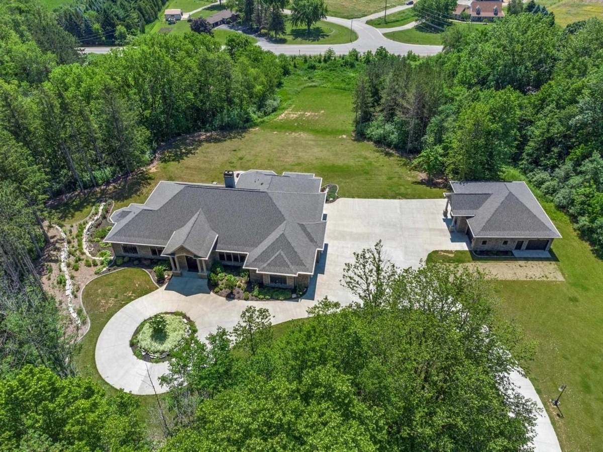 Aerial view highlights the house, a detached garage, a circular driveway, and a spacious yard surrounded by trees.