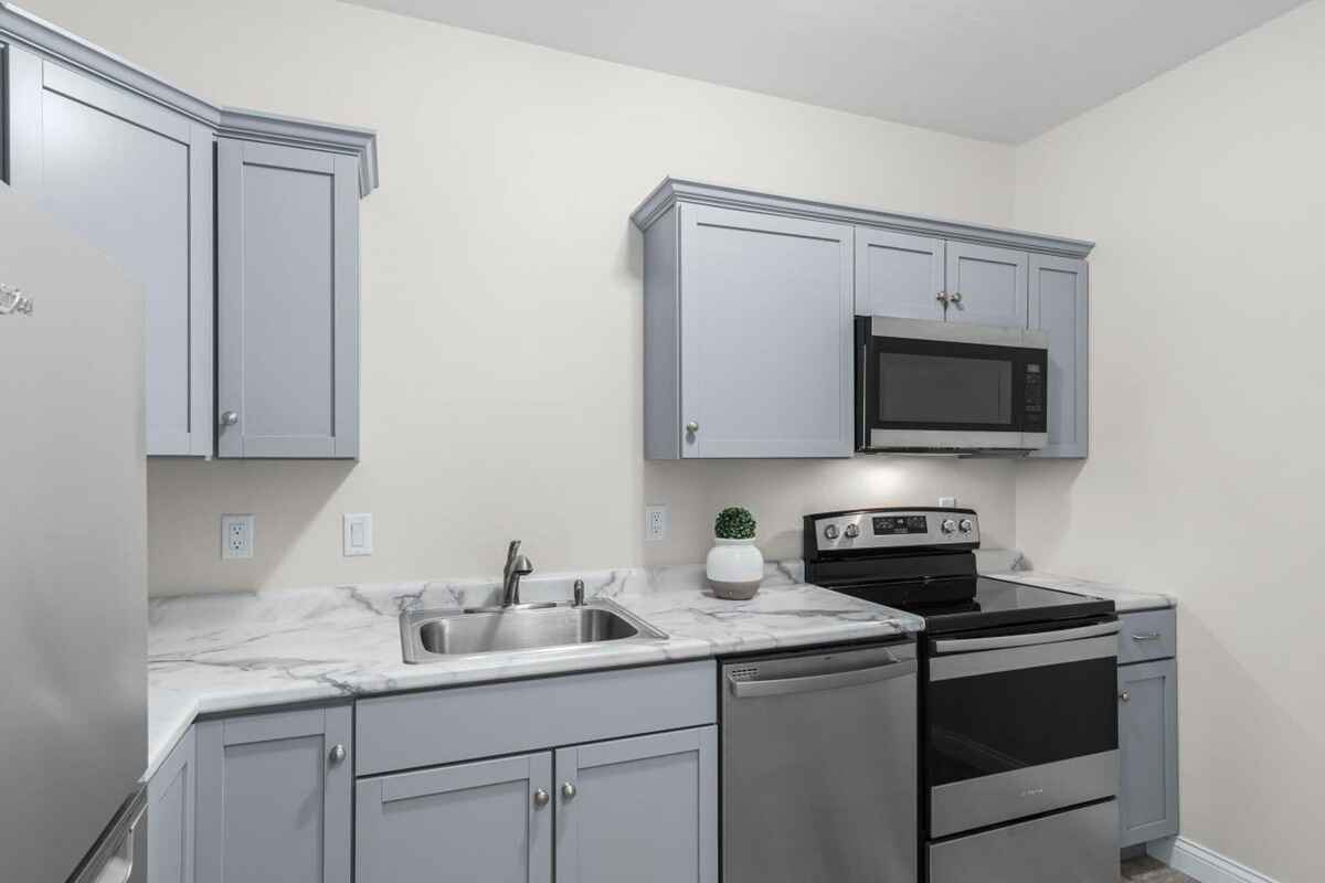 Kitchenette has light gray cabinets, marble countertops, and stainless steel appliances.