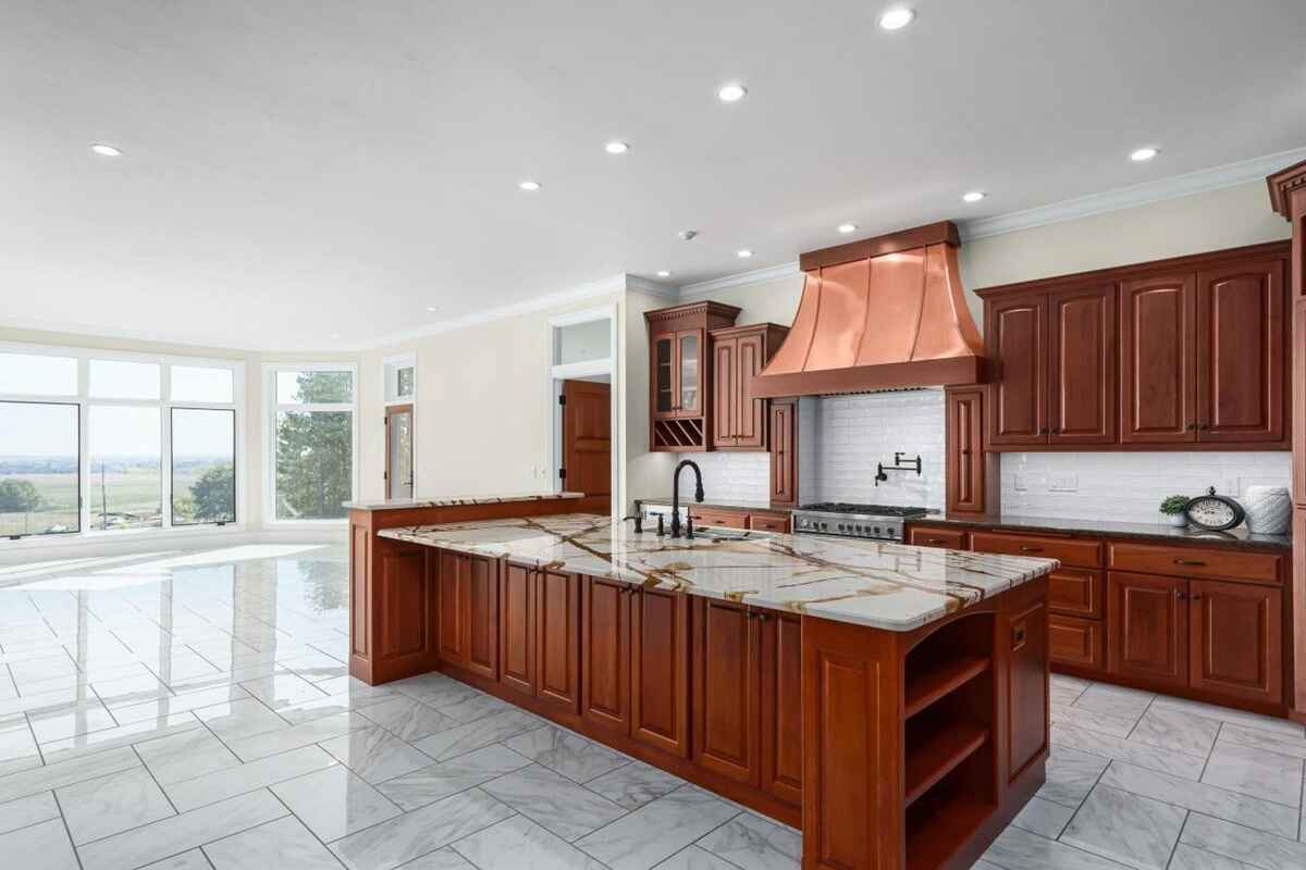 Main kitchen includes a large island with marble countertop, copper range hood, and wooden cabinetry.