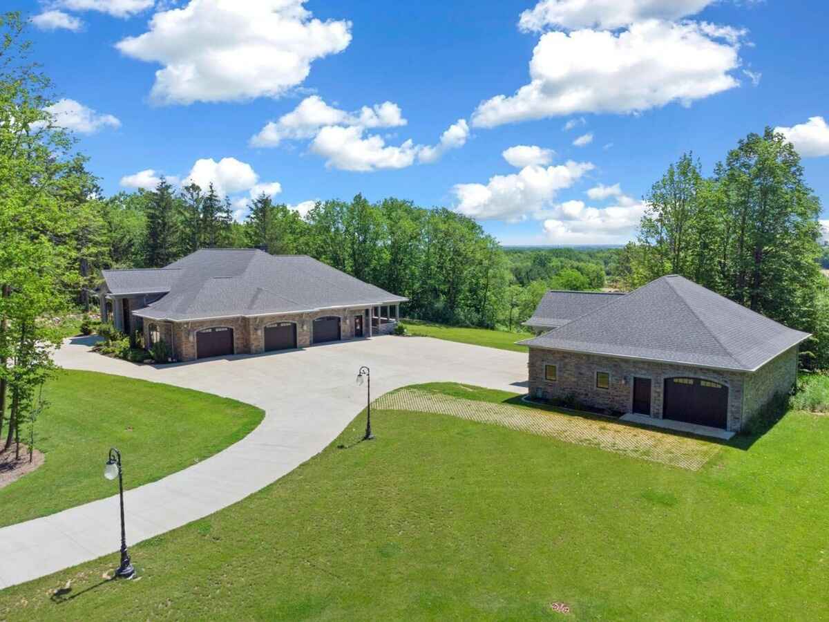 Driveway leads to a side view of the house with a three-car garage and a detached structure in the background.