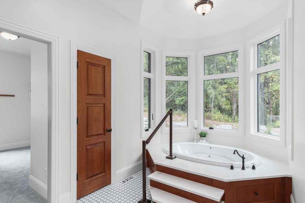 Bathroom features a large soaking tub with steps, bay window, and wood door leading to another room.