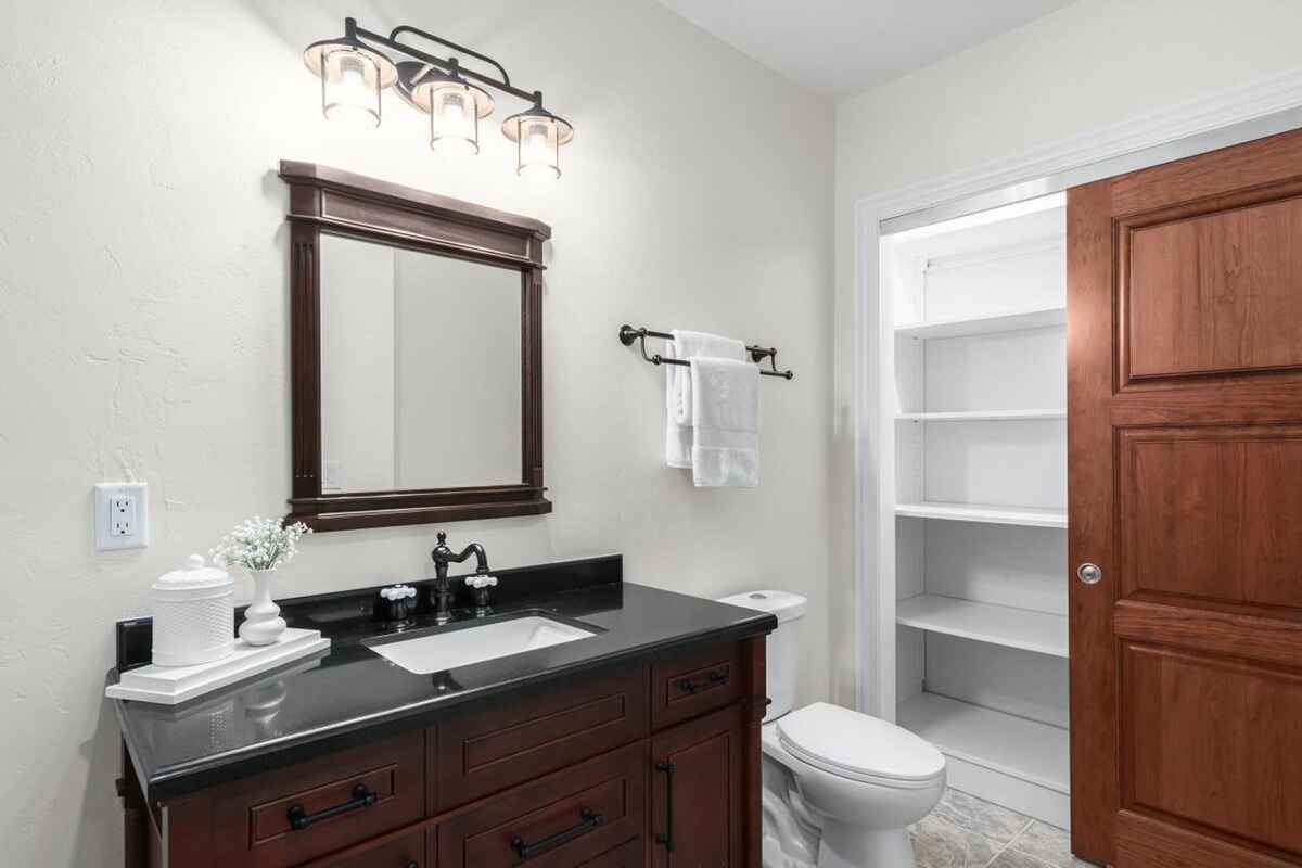 Bathroom features dark wood vanity with black countertop, a framed mirror, and a linen closet with a sliding door.