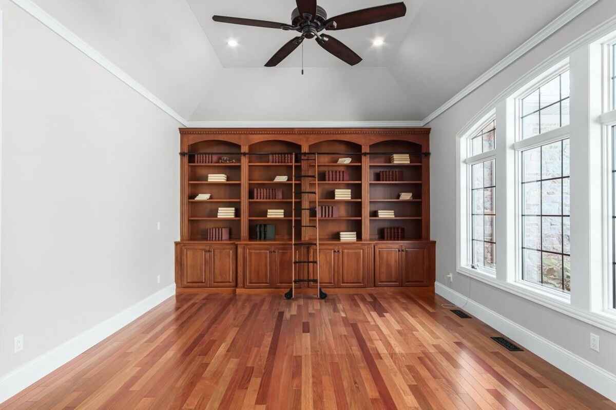 Room features hardwood floors, large windows, and a built-in wooden bookcase with a rolling ladder.