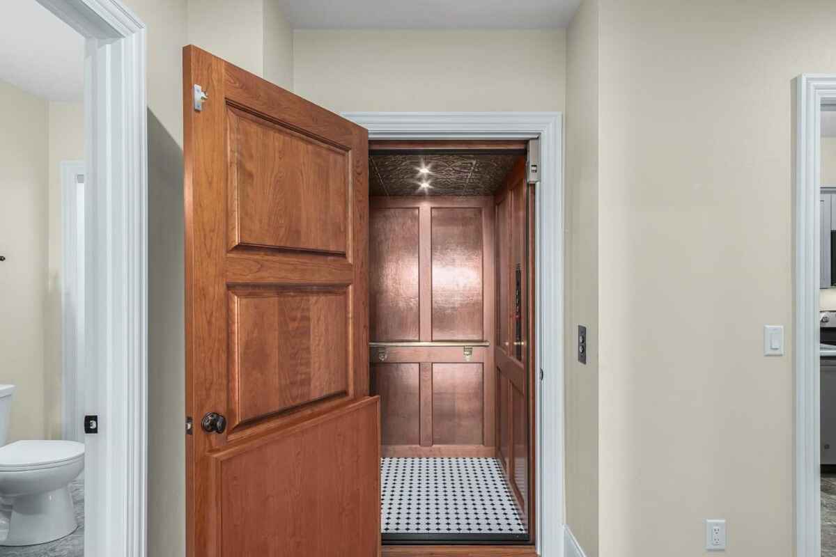 Home features a private elevator with a wood door partially open, revealing a copper-colored interior and black and white tiled floor.