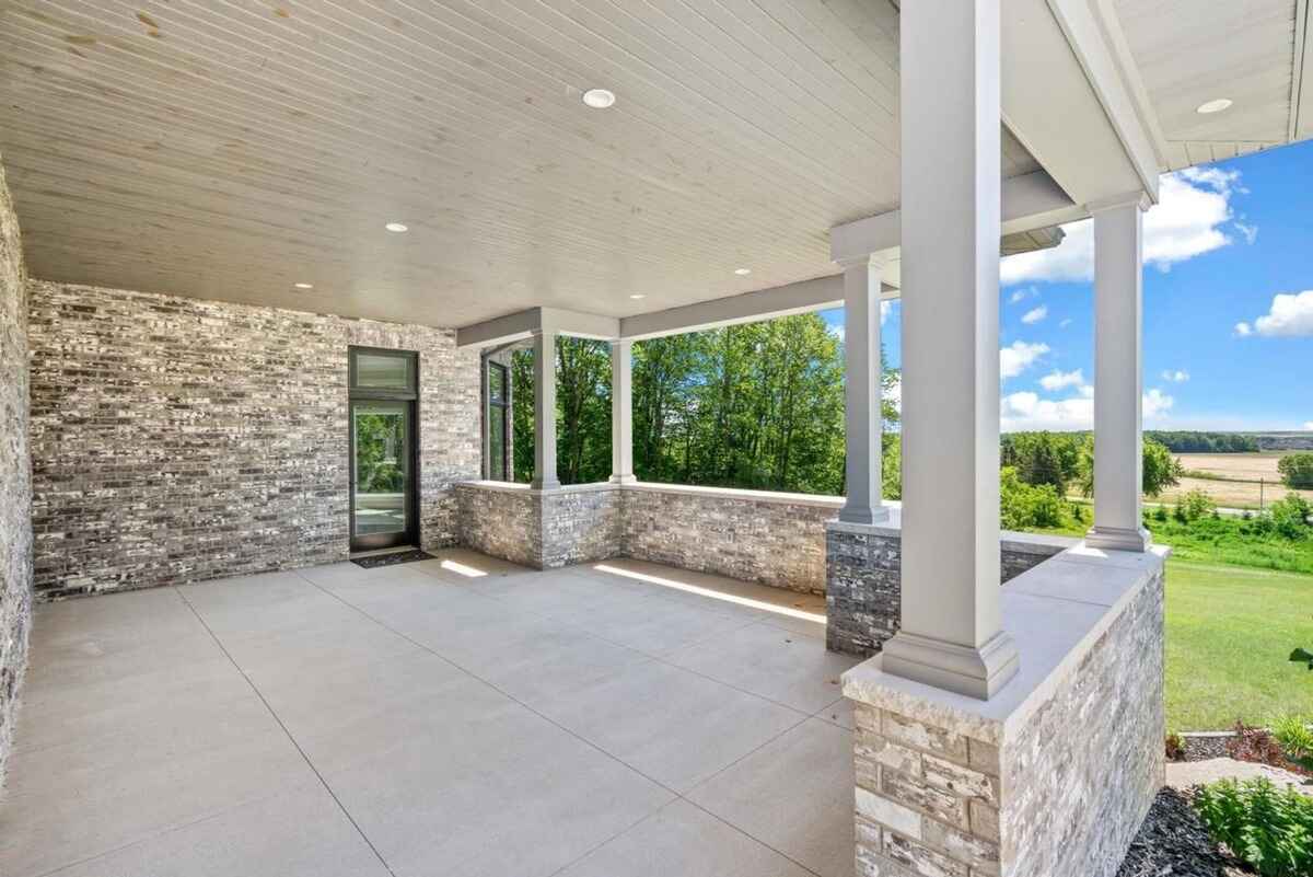 Spacious covered patio includes stone accents, ample space for seating, and views of the lush greenery.