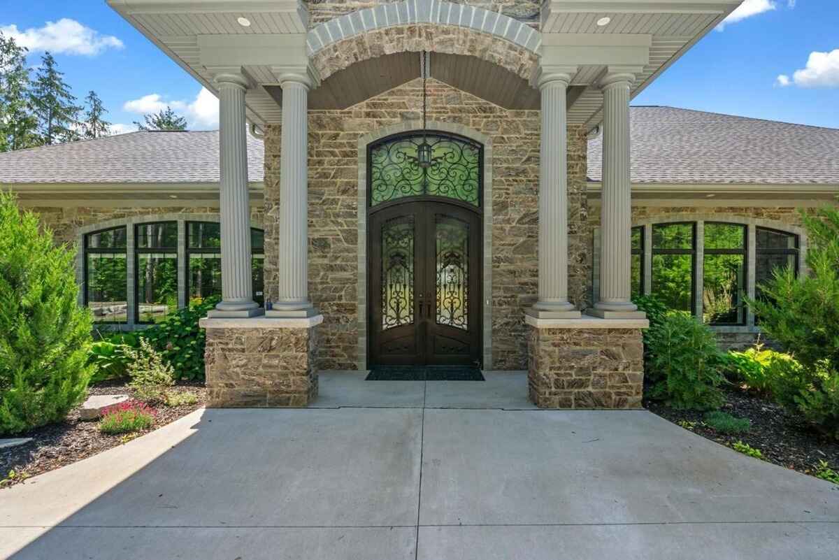 Close-up displays the main entrance with decorative wrought iron doors and stone pillars under a covered porch.