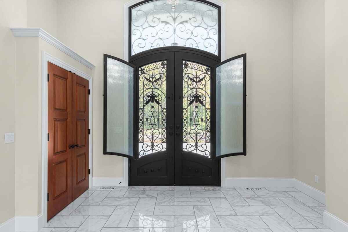 Interior foyer showcases a double iron door with glass panels, marble floors, and a nearby wooden closet.