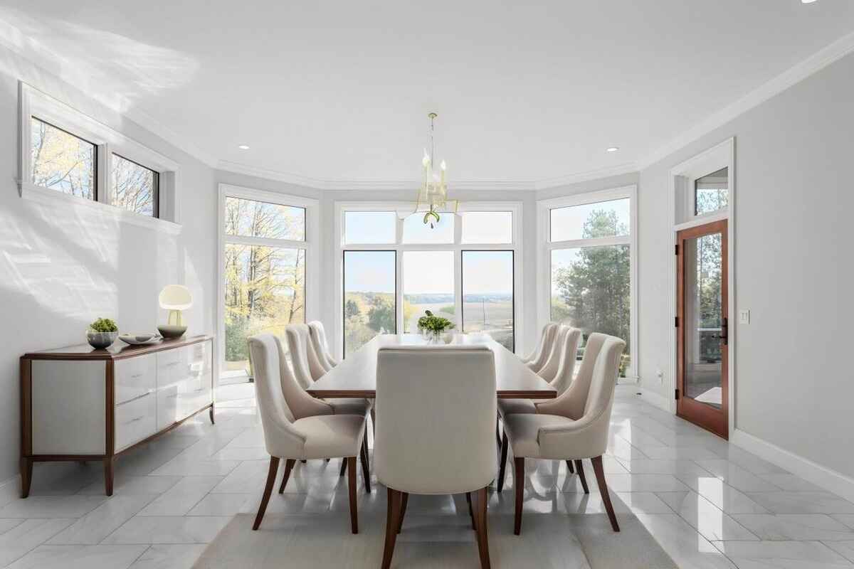 Dining room has a long table with upholstered chairs, large windows, and views of the outdoors.