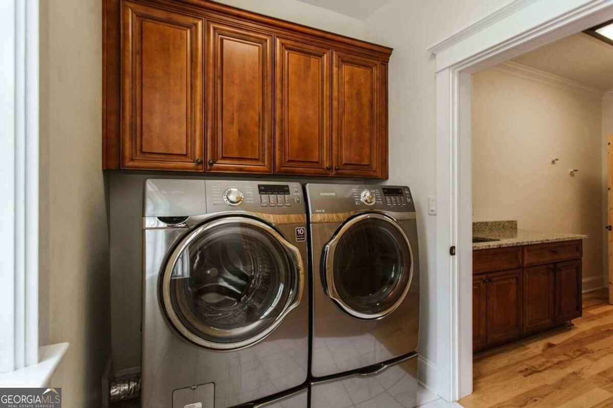 Laundry room includes modern front-loading washer and dryer beneath built-in wooden cabinets.