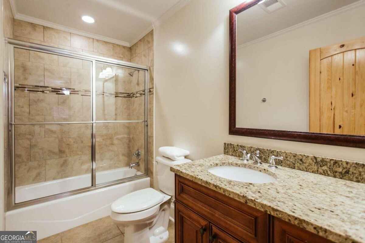 Bathroom features granite countertops, wooden cabinetry, and a tiled shower-bathtub combination with glass enclosure.