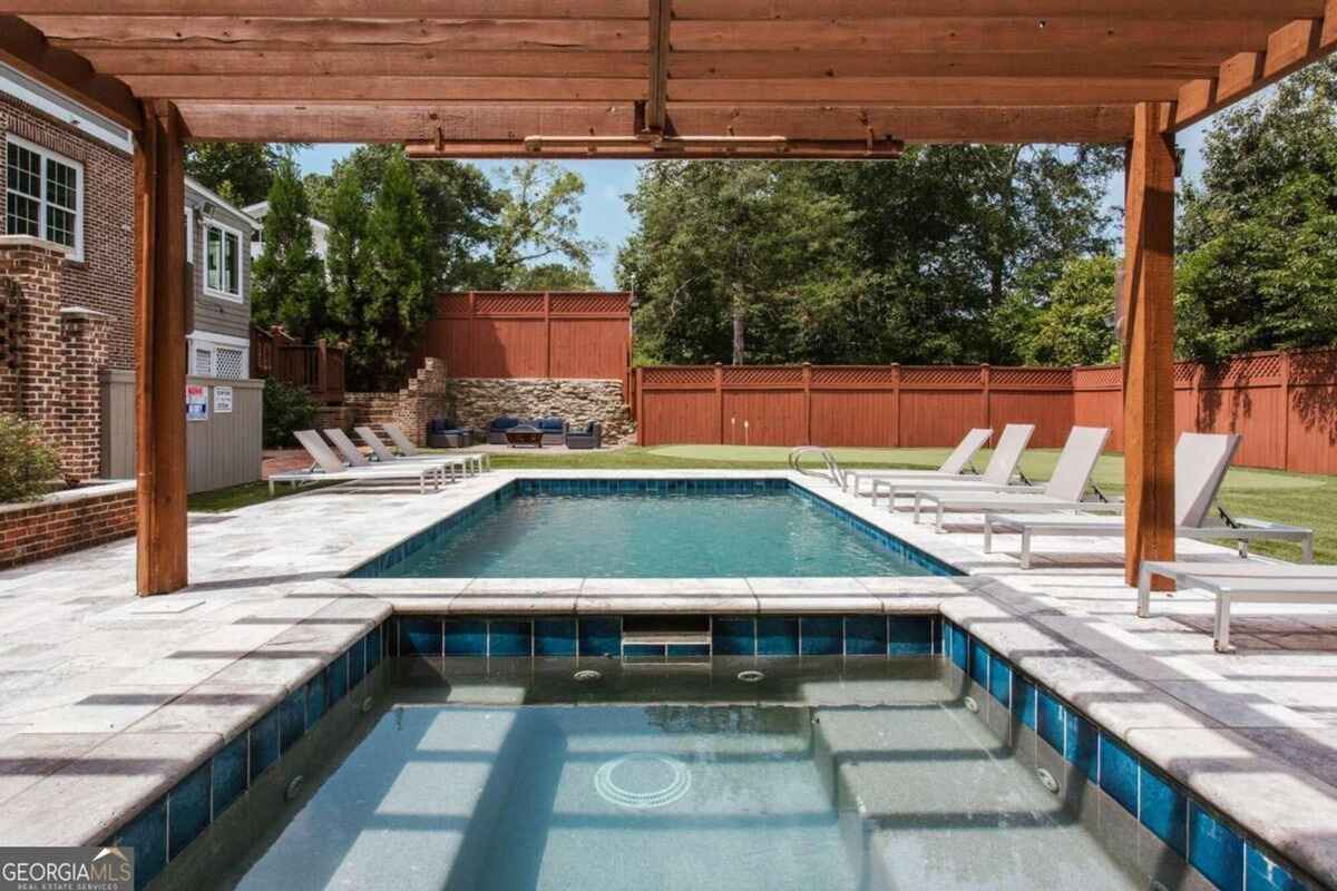 Pool and spa combination are framed by a pergola and surrounded by a stone deck.