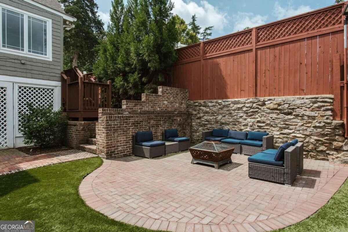 Brick-paved patio includes outdoor seating and a fire pit against a stone and wood fence.