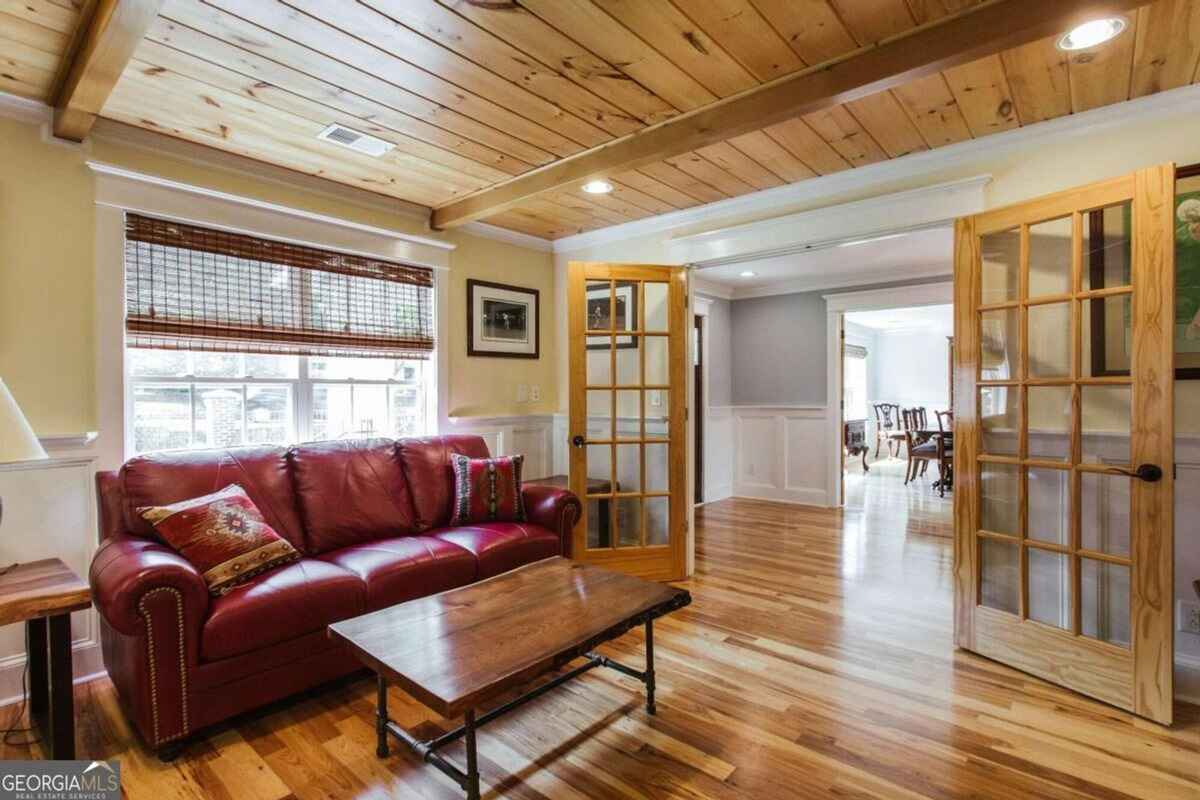 Cozy living space displays a wood-paneled ceiling, a red leather sofa, and French doors connecting to other areas.