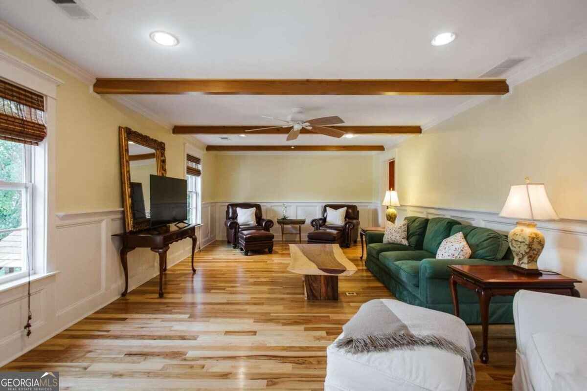 Living room features a long green sofa, leather chairs, and exposed ceiling beams.