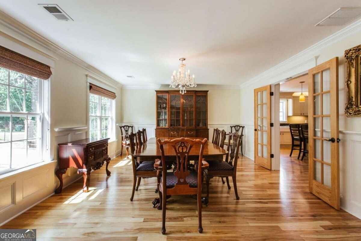 Dining room showcases a wooden table, chandelier, and large china cabinet with natural light.