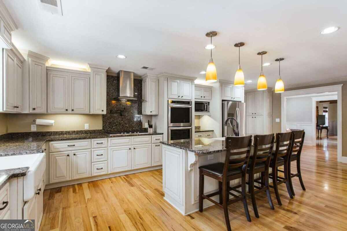 Spacious kitchen includes white cabinetry, granite countertops, and a central island with pendant lighting.