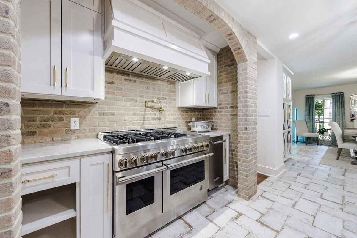 Cooking area includes a double oven range, custom hood, and exposed brick archways.