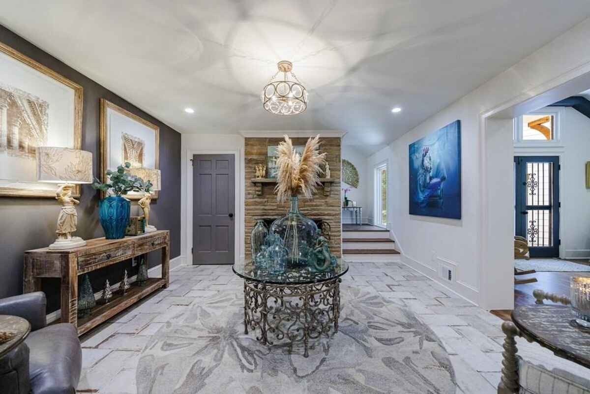 Entryway features a rustic console table with decorative accents, a central glass-top table, and a stone accent wall with a fireplace mantel. 