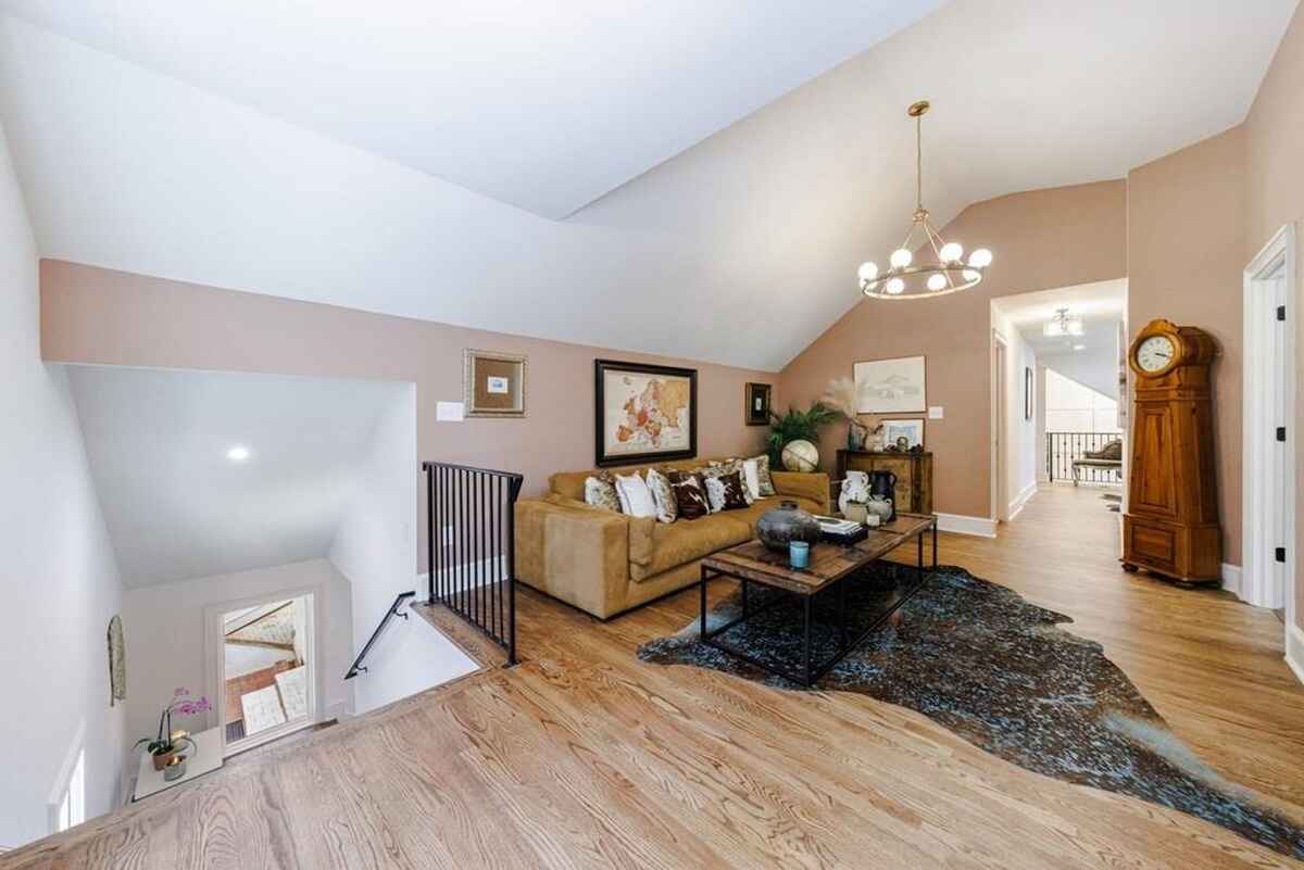 Living space includes a sloped ceiling, beige sofa, wall decor, and a modern chandelier above a wooden floor with an accent rug.