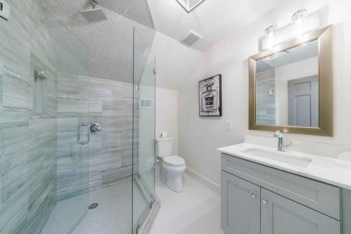 Bathroom includes a glass-enclosed shower, light gray vanity, and contemporary lighting with neutral wall tones.