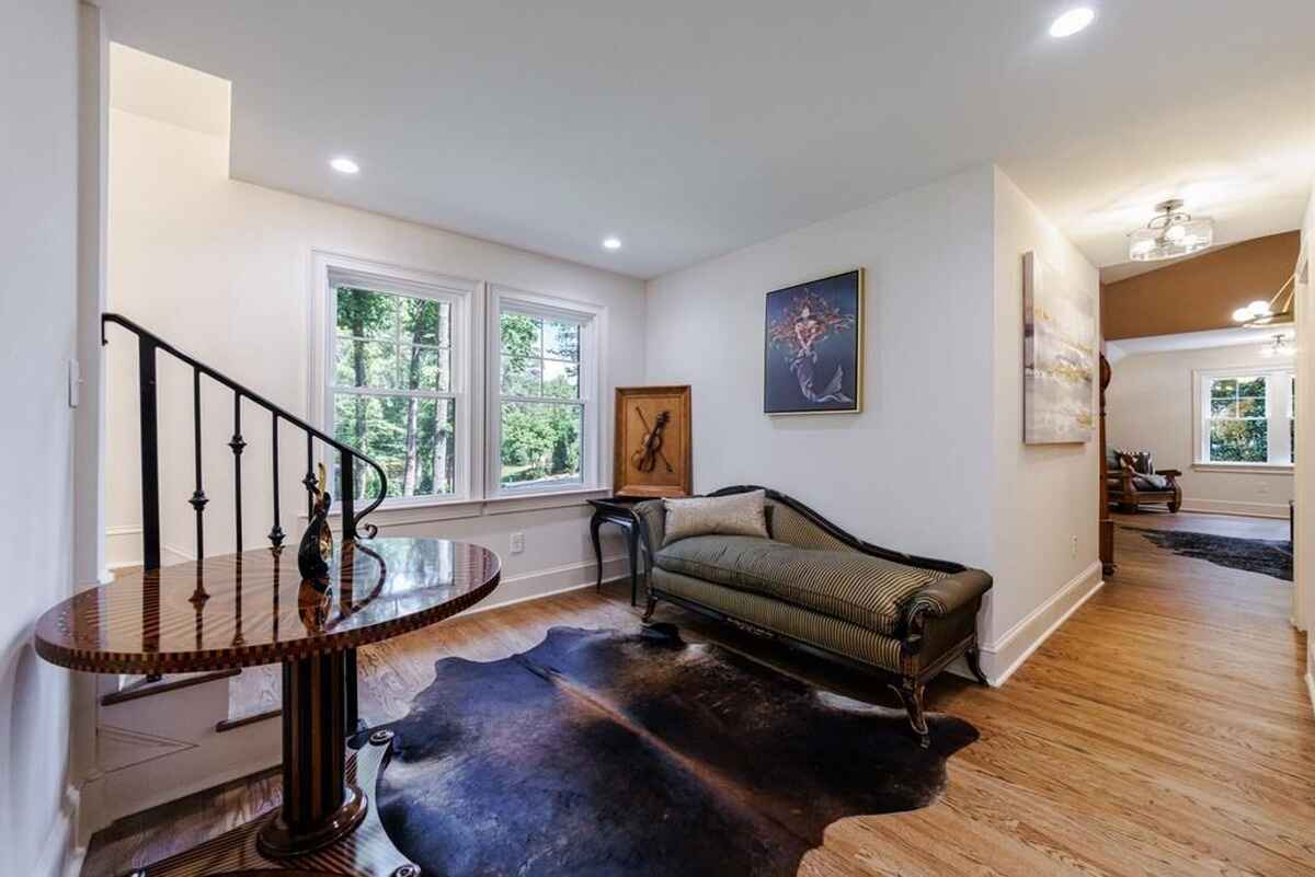 Entryway features a curved staircase with black metal railing, a small table, a chaise lounge, and a window overlooking greenery.