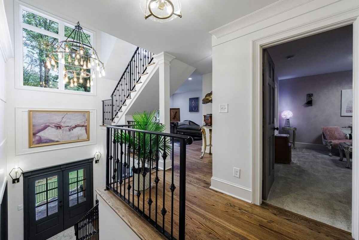 Staircase landing includes a large window, a chandelier, and a black metal railing with access to multiple rooms.