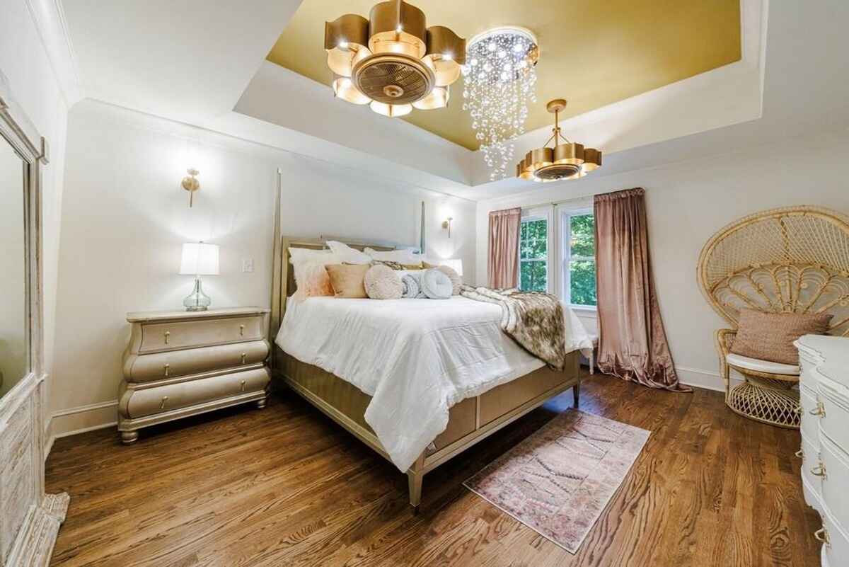 Bedroom showcases a tray ceiling with two light fixtures, a bed with white bedding, and warm-toned decor.