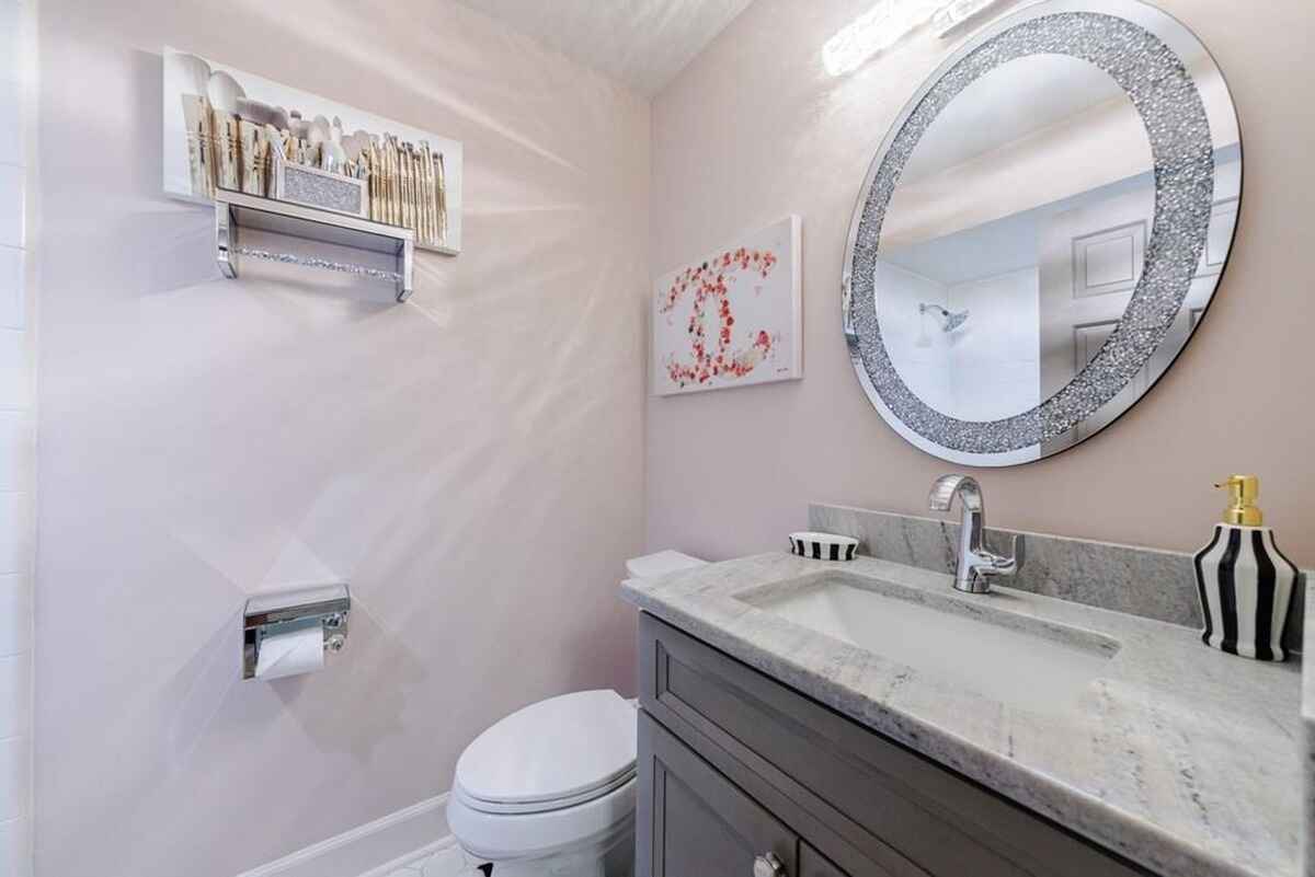 Powder room features a round mirror with glitter detailing, a small vanity, and light pink walls.