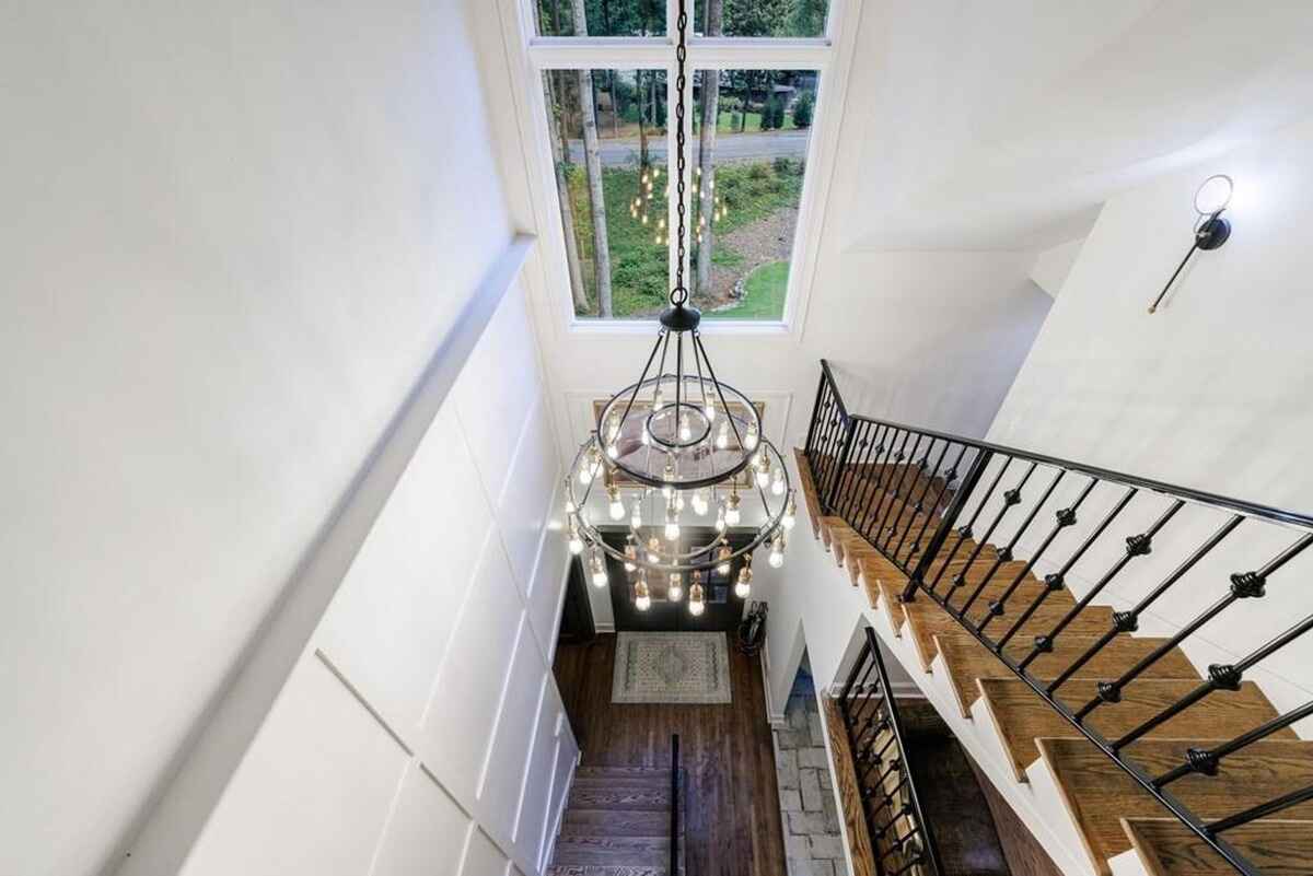 Stairwell view shows a large chandelier, black metal railing, and a window overlooking greenery.