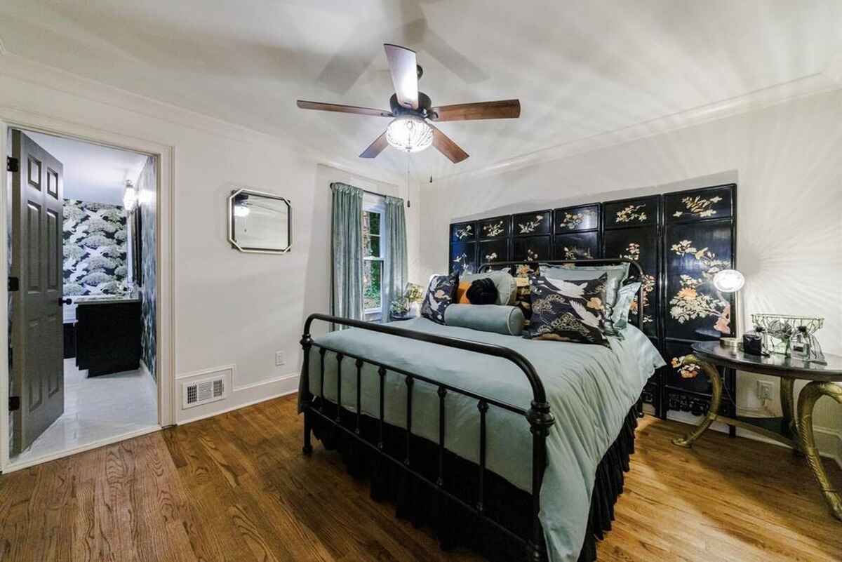 Hardwood floors, a ceiling fan, and a bed with an ornate headboard create a serene bedroom.