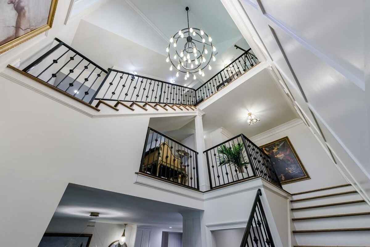 Central staircase design displays multiple levels, black iron railings, and a chandelier with circular lights.