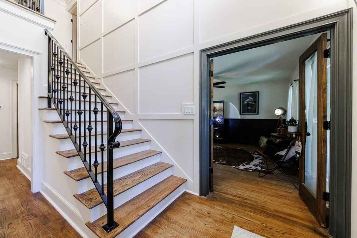 Staircase includes wooden steps, iron railings, and opens to a study with glass double doors and dark trim accents.